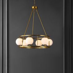 a chandelier with five lights hanging from it's center, in front of a dark wall