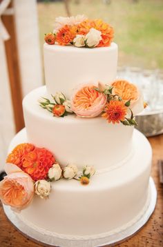 a three tiered white cake with orange and white flowers