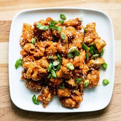 a white plate topped with meat covered in sesame seeds and green onions on top of a wooden table