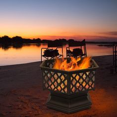 a fire pit sitting on top of a sandy beach next to the ocean at sunset