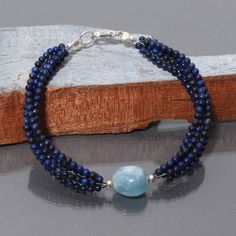 a bracelet with blue beads and a beaded clasp on a piece of drift wood