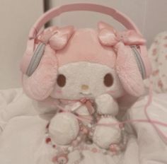 a white stuffed animal with headphones on sitting next to a pink teddy bear in bed