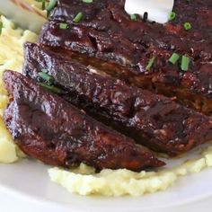 some meat and mashed potatoes on a white plate with green onion garnish