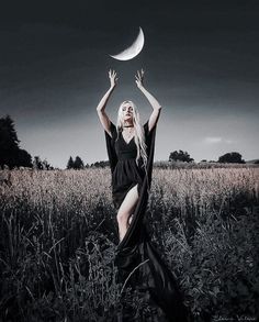 a woman in a black dress is holding a half moon above her head while standing in a field