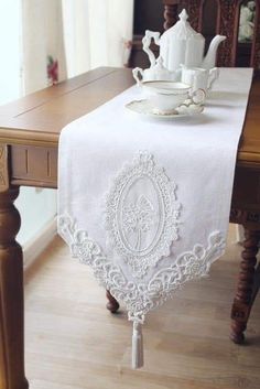 a white table runner on top of a wooden table with a cup and saucer