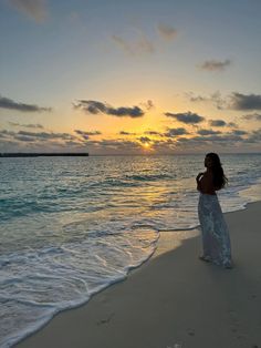 a woman standing on top of a sandy beach next to the ocean at sun set