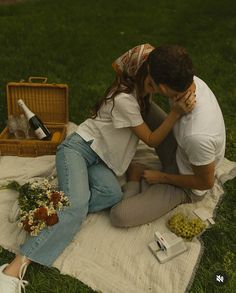 a man and woman are sitting on a blanket in the grass with wine bottles, flowers and other items