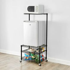 a white refrigerator sitting on top of a metal rack next to a wall and wooden floor