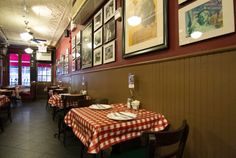 an empty restaurant with red and white checkered tablecloths on the tables in front of framed pictures