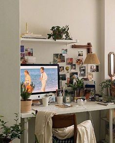 a desk with a computer monitor and pictures on the wall next to potted plants