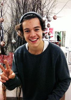 a young man is making the peace sign with his hand while standing in front of a christmas tree