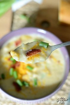 a spoon full of soup with cheese and green onions on the side in a purple bowl