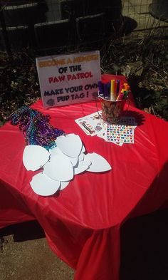 a red table topped with paper cutouts and other crafting supplies next to a sign that says out of the paw patrol make your own pup taco