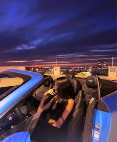 a woman sitting in the driver's seat of a sports car at night time