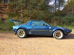 a blue sports car parked on the side of a dirt road in front of trees