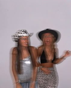 two women standing next to each other in front of a white wall and wearing hats