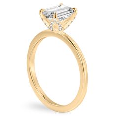 a yellow gold engagement ring with an emerald cut diamond in the center and side stones