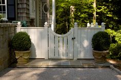 a white gate with two potted plants on the side and an open window above it