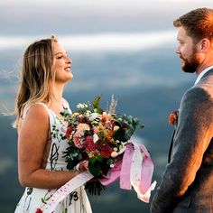 a man and woman standing next to each other with flowers in their hands, looking at each other