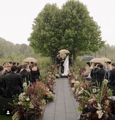 an outdoor wedding ceremony with umbrellas and flowers on the aisle, surrounded by people holding umbrellas