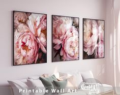 three pink flowers are hanging on the wall next to a couch in a living room