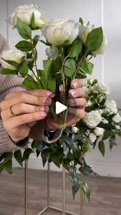 a woman is arranging white roses in a vase with greenery on the side and her hands holding it