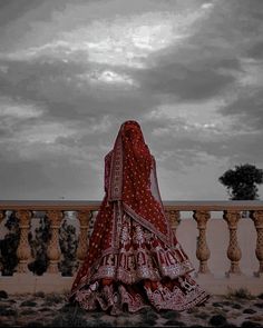 a woman in a red and white bridal gown standing on a balcony looking at the sky