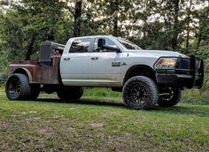 a large white truck parked on top of a lush green field with trees in the background