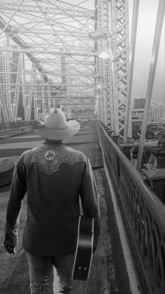 a man walking across a bridge with a guitar in his hand while wearing a cowboy hat