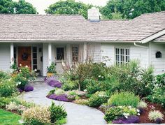 a white house with lots of flowers and plants around it's front door area