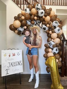 a woman holding a small child in front of a balloon arch with soccer balls on it