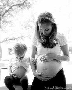 a pregnant woman sitting next to her baby bumping it's belly in front of a window