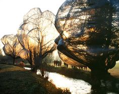 some people are walking by the water with large sculptures on it's sides and trees in the foreground