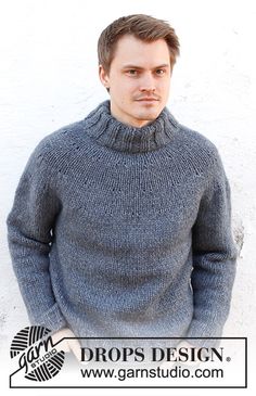 a man wearing a gray sweater standing in front of a white wall with the words drops design on it