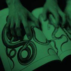 two hands on top of an open book with green light in the background and black and white image