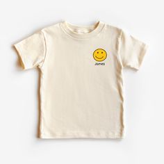 a white t - shirt with a yellow smiley face on the chest and name james