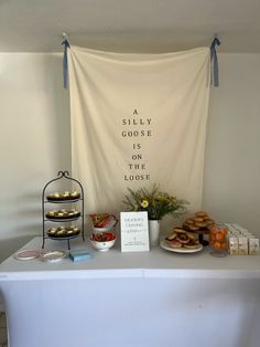 a table topped with donuts and pastries next to a white banner that says, a silly goose is in the loose