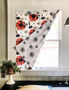 a kitchen window with red and black flowers on the valance, next to a potted plant