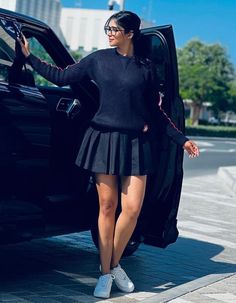 a woman in a black sweater and skirt getting out of a car