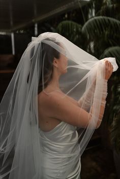 a woman in a white dress is holding a veil over her head and looking at something