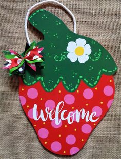 a welcome sign hanging from the side of a wall with a flower on it's head