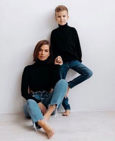 two people sitting on the ground with one person standing up in front of them and another woman leaning against the wall