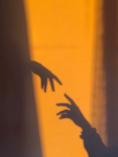 the shadow of a hand reaching out to another person's arm, in front of a yellow wall