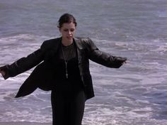 a woman standing on top of a beach next to the ocean holding her arms out