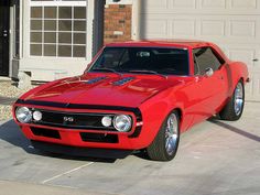 a red muscle car parked in front of a garage