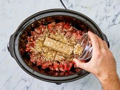 a person pouring something into a crock pot filled with meat and other food items