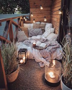 a bed with pillows and blankets on top of it next to some plants, candles and potted plants