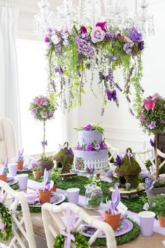 the table is set with purple and white flowers, greenery, and fairy cakes