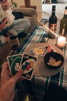 two people sitting on a couch holding cards and drinking wine in front of the camera