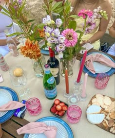 the table is set with pink and blue plates, wine bottles, flowers, and other items